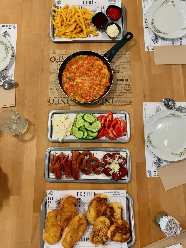 Üstten çekilmiş kahvaltı: menemen, patates, peynir, söğüş ve sıcaklar